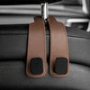 Two brown leather car headrest hooks with black grips hanging from a metal clip.