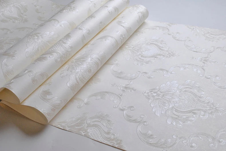 Rolls of embossed damask wallpaper featuring a textured floral design on white fabric.