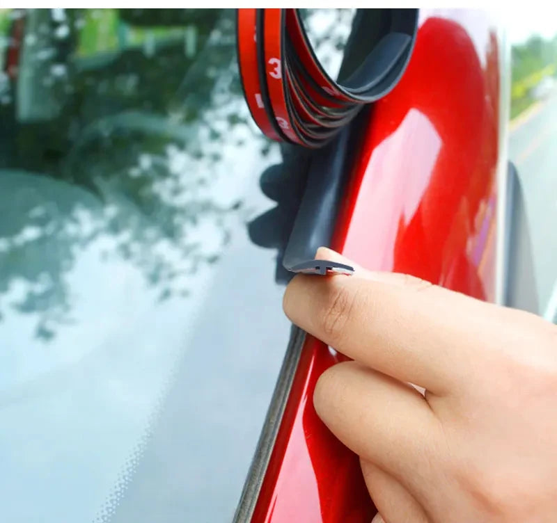 A hand is applying a black rubber seal strip to the edge of a red car window frame.