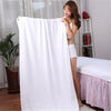 A woman models a large white microfiber bath towel draped over her body in a bright indoor setting.