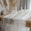 Elegant faux pearl tulle table runner draped over a wooden table with white candles and dried grasses.
