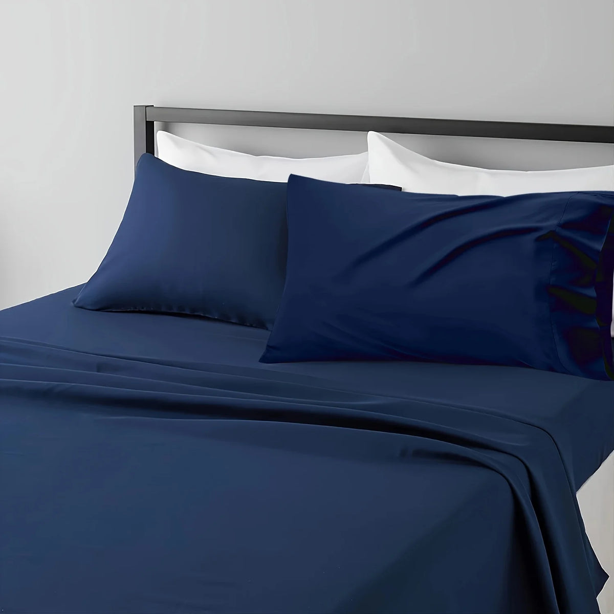 A dark blue microfiber bed sheet set with white pillows and a gray headboard.