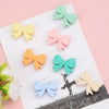 A collection of pastel silicone bow beads in mint green, pale yellow, pink, and light blue arranged on a white surface.