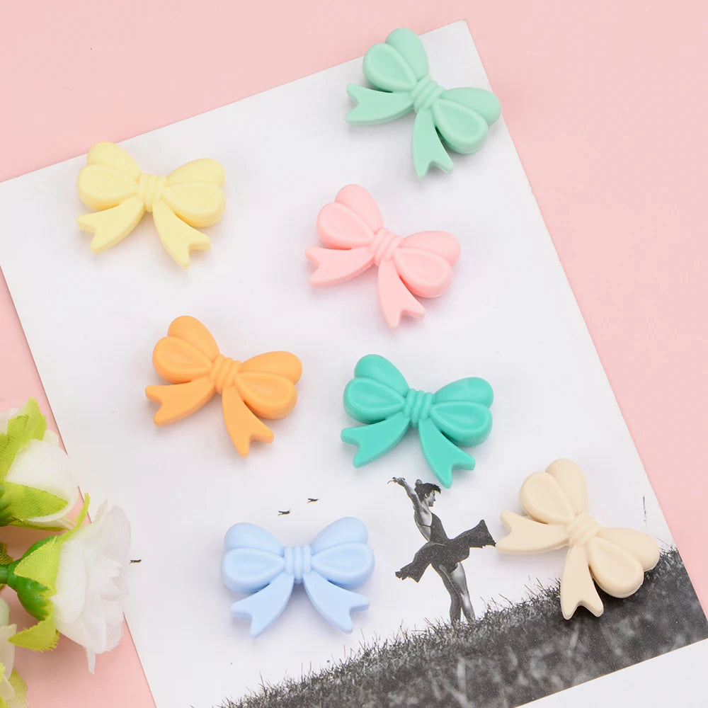 A collection of pastel silicone bow beads in mint green, pale yellow, pink, and light blue arranged on a white surface.