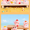 Pink resin pig figurines in various poses and colors displayed on a wooden surface with yellow sand.