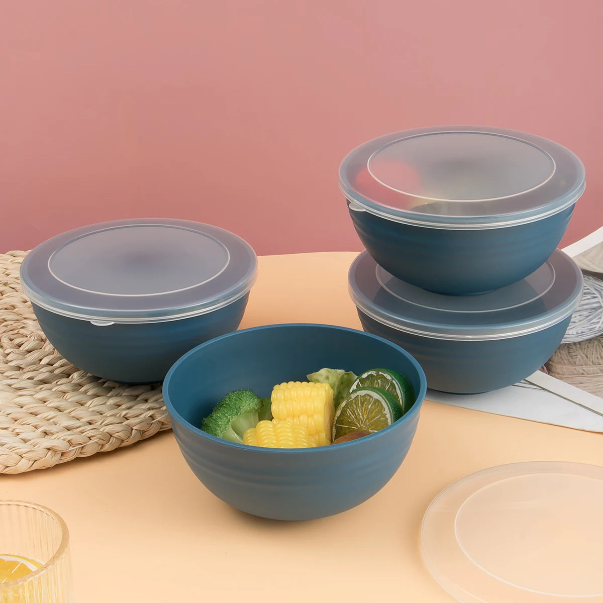 A set of three matte blue airtight storage bowls with lids, containing sliced cucumbers and corn.