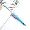 A close-up of a sparkly blue ballpoint pen with a sequin accent, resting on white paper.