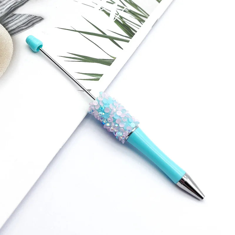 A close-up of a sparkly blue ballpoint pen with a sequin accent, resting on white paper.