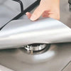 A hand is placing a silver reusable gas stove burner protector onto a stovetop grate.