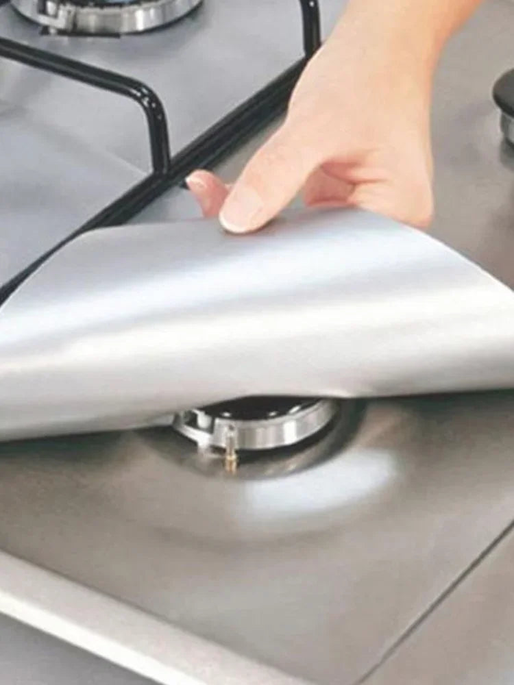 A hand is placing a silver reusable gas stove burner protector onto a stovetop grate.