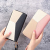 A hand holds a long zip-around PU leather wallet with card slots featuring black, beige, and pink panels.