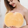 A woman holds a yellow silicone shower mat with exfoliating bristles against her bare shoulder.