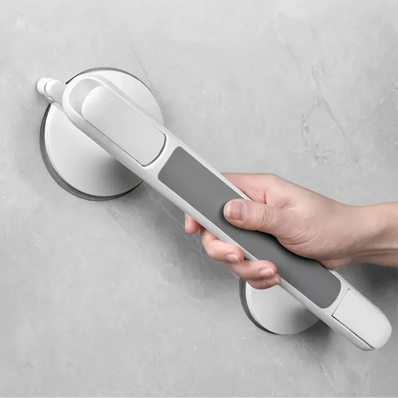 A hand is holding a white and gray non-slip suction grab bar designed for bathroom safety.