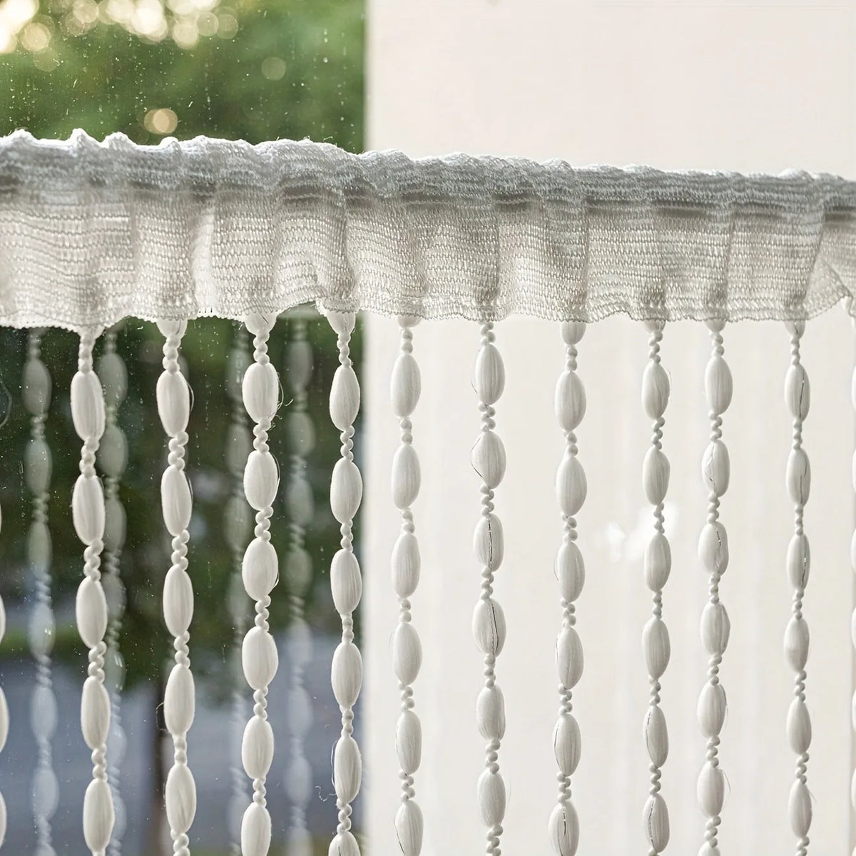 White bohemian tassel curtain with elongated white lanterns hanging in front of a window.