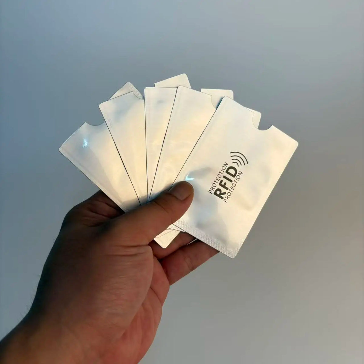A hand holds a stack of white RFID blocking card sleeves with geometric patterns.