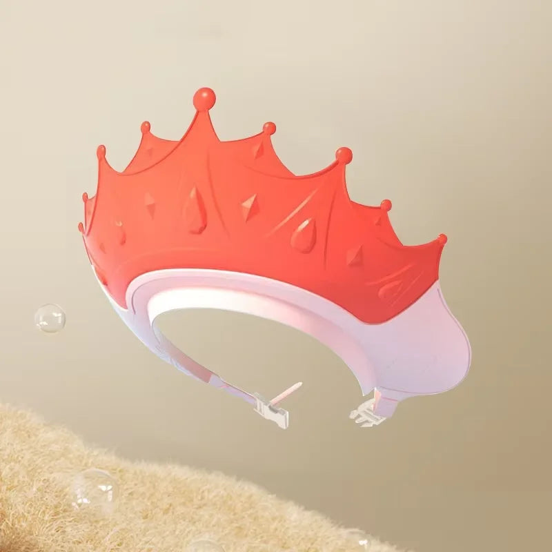 An orange and white adjustable baby bath shampoo shield cap with a crown design is shown against a light background.