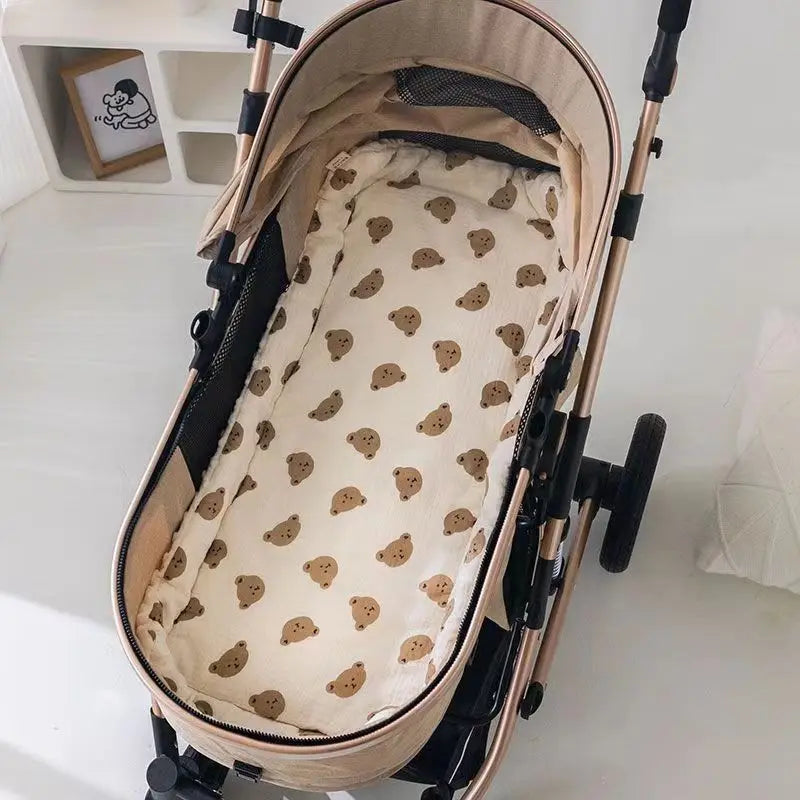 A beige padded seat cushion for a baby stroller, featuring a light fabric and brown accents.