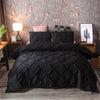 Black quilted comforter and pillowcases displayed on a bed with string lights in a bedroom setting.