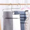 A silver S-shaped pants hanger with multiple bars is shown holding a gray towel, a white towel, and a blue shirt on a rack.