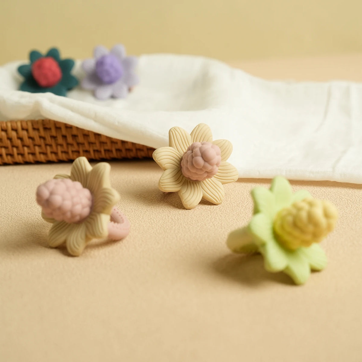 Silicone baby teether toys shaped like flowers and grapes in pastel colors on a beige surface.