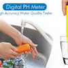 A hand holds a yellow digital pH meter testing water in a glass, with an orange carrot visible nearby.