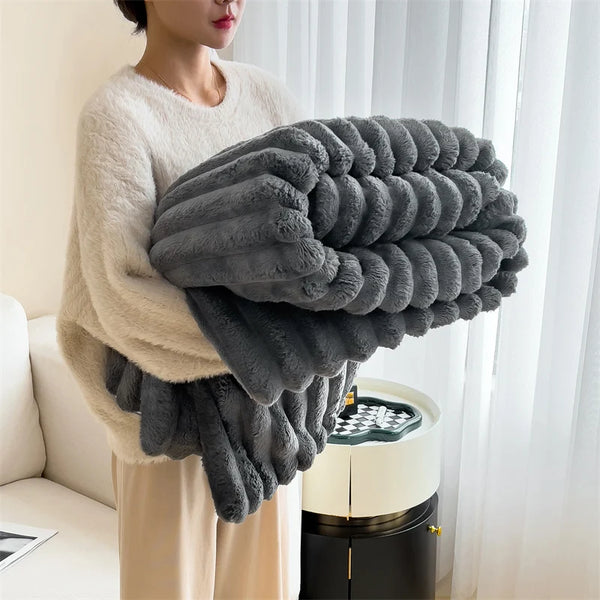 Una persona sostiene una gruesa manta de peluche gris frente a una ventana blanca.
