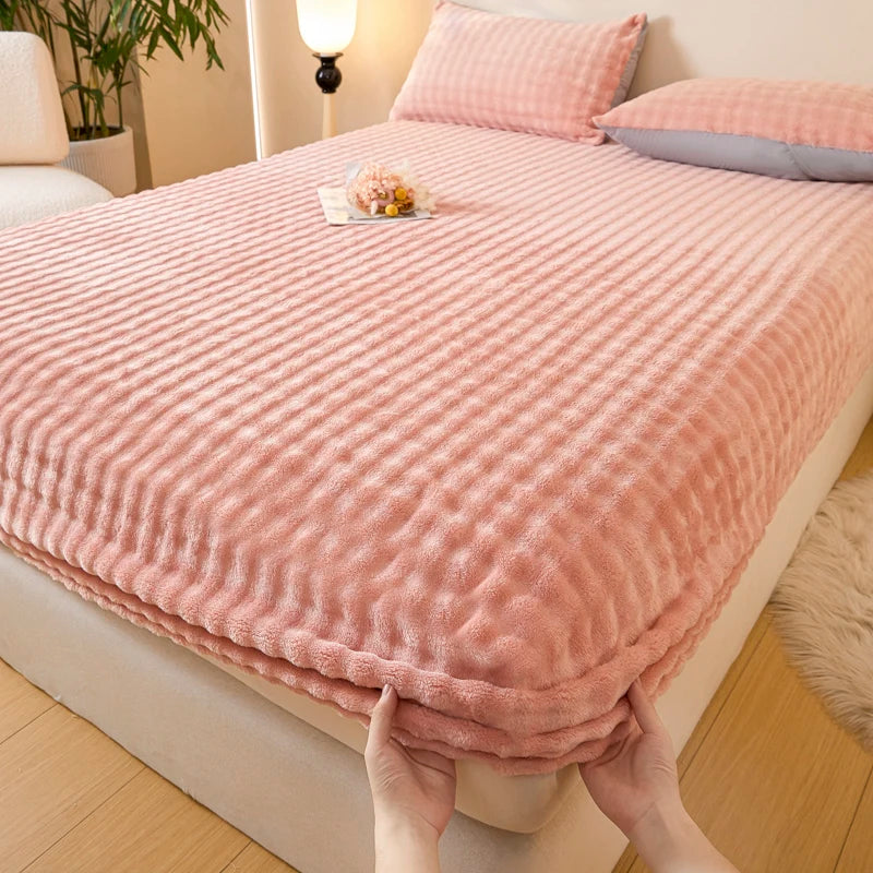 A pink quilted faux fur fitted sheet is being held up on a bed, showing its texture and fit.