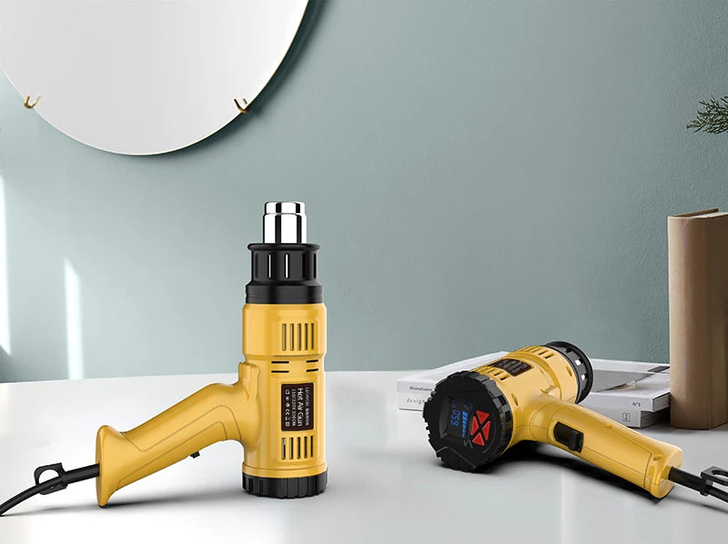A yellow heat gun is shown on a white surface against a light blue wall, with another similar tool nearby.