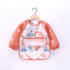 A pink waterproof long-sleeve baby feeding smock with orange stripes and blue accents, hanging on a wooden hanger.