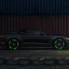 A dark gray sports car with bright green reflective wheel stickers parked on a rough ground.
