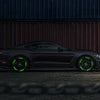 A dark gray sports car with glowing green reflective wheel stickers parked on asphalt.