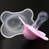 A pink silicone baby pacifier with a flower design and protective cover is shown against a dark background.
