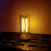 A glass LED night light with a warm filament glow sits on a dark metal grate.