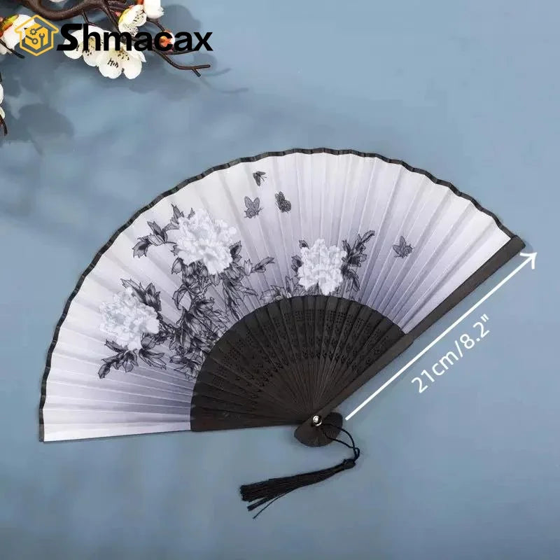 A black and white bamboo and silk folding fan with a floral design shown against a light blue background.
