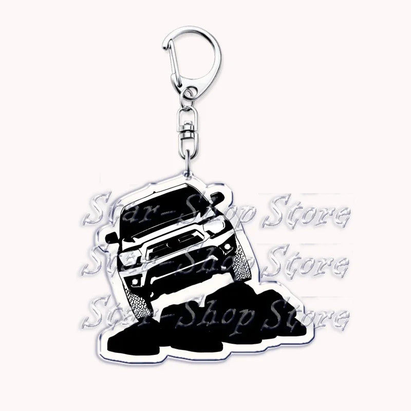 A silver metal key ring with a detailed off-road truck charm featuring a vehicle silhouette on a pile of black rocks.