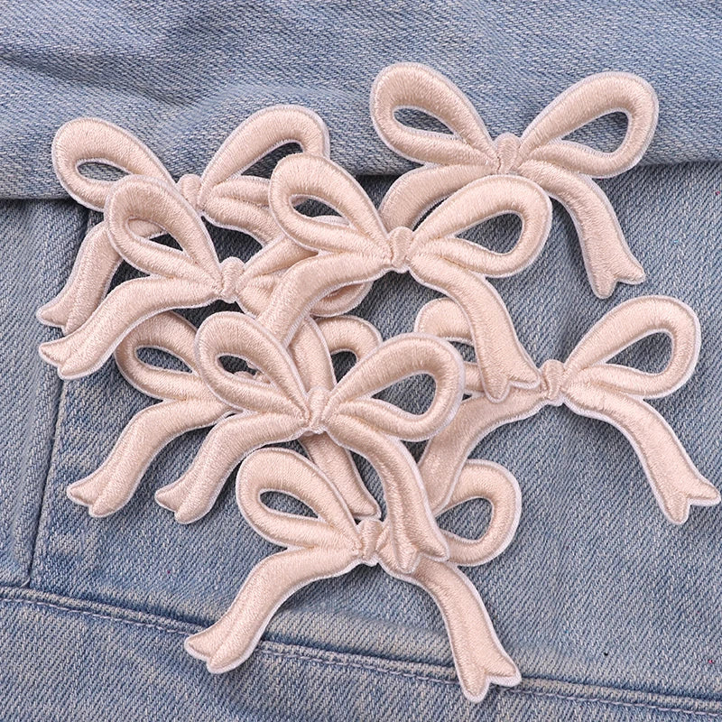 Light pink embroidered cartoon bow iron-on patches sewn onto a denim fabric.