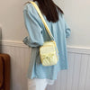 A light blue oversized shirt is worn by a person carrying a pale yellow bow-decorated casual crossbody bag.