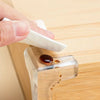 A hand wipes a silicone corner edge guard on a wooden surface, demonstrating its waterproof and easy-to-clean features.