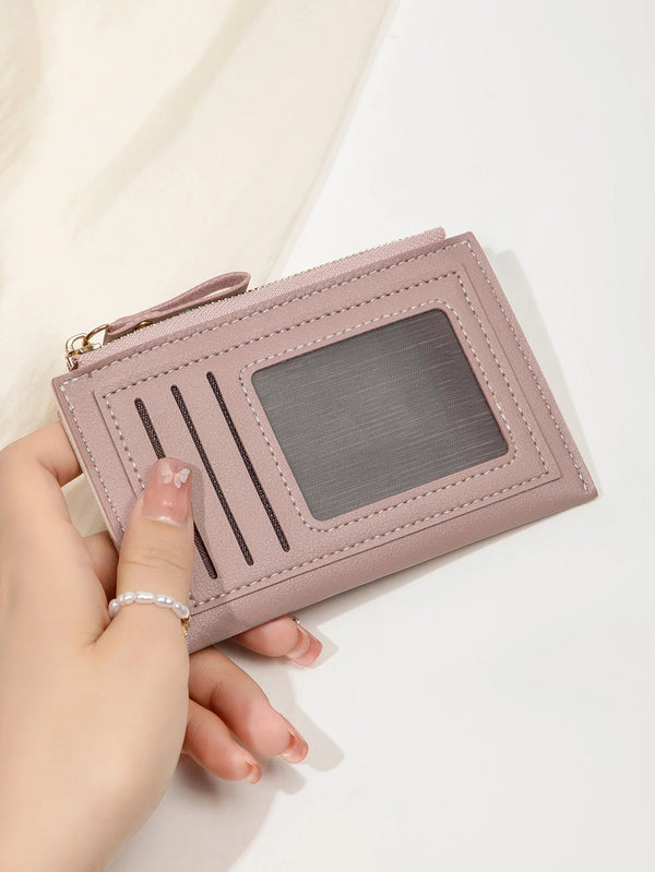 A hand holds a light pink slim leather card holder wallet with a secure zipper and a clear plastic window.