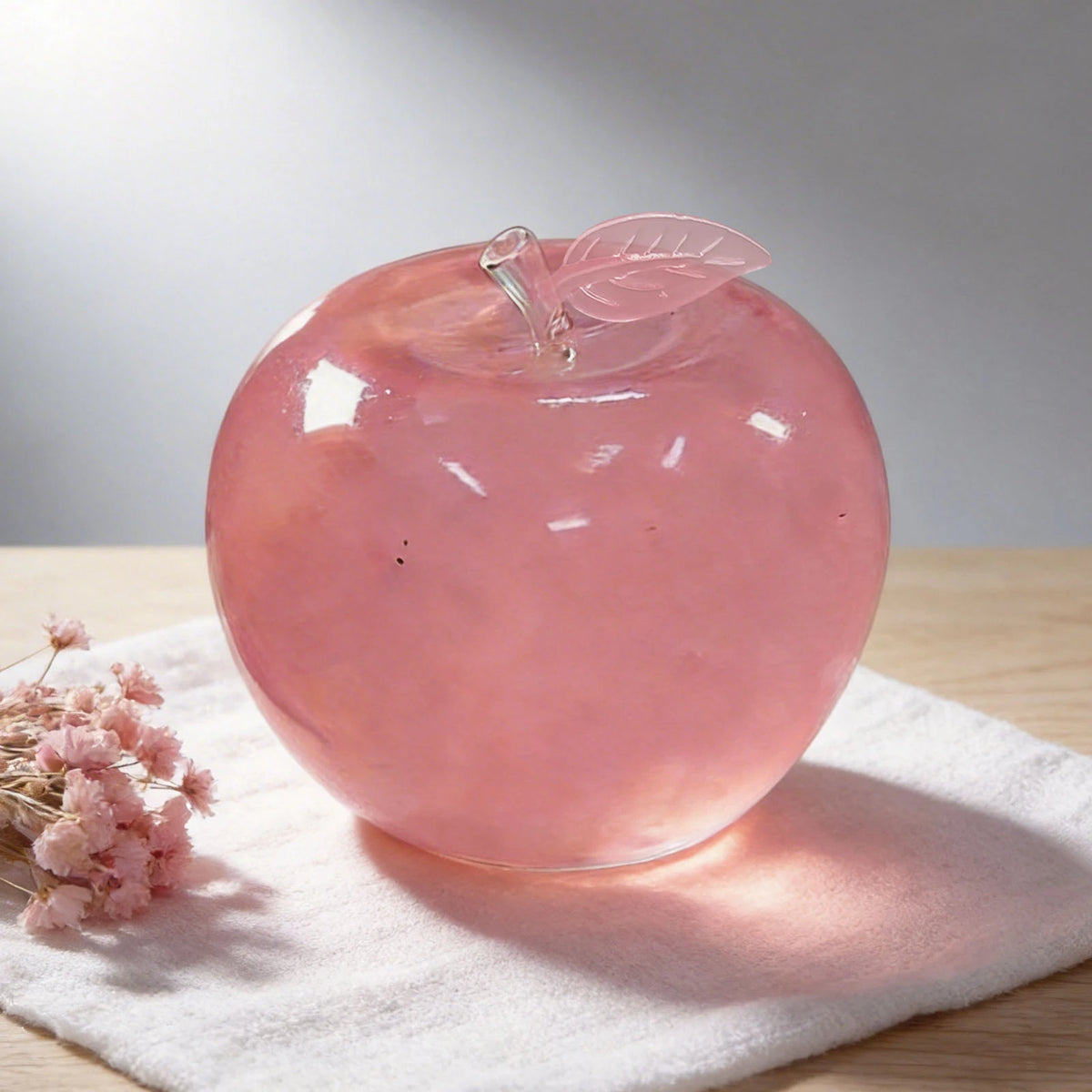 Eine glatte, rosa Glas-Apfel mit Blatt oben auf einem weißen Handtuch.