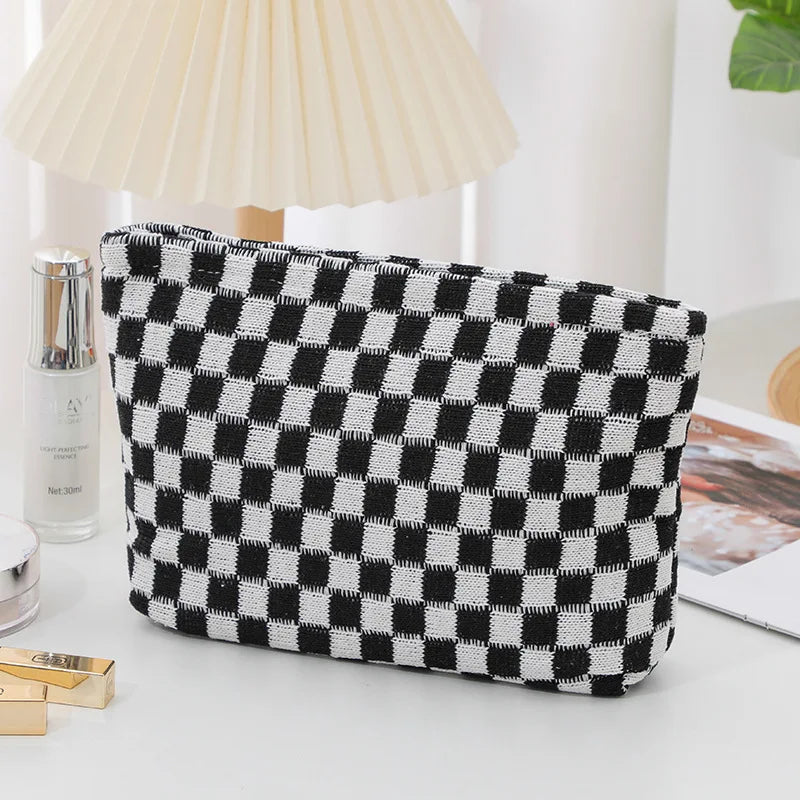 A black and white checkered plaid makeup bag with a zipper resting on a white surface.