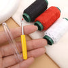A hand holds a stainless steel sewing needle and several spools of colored thread for heavy-duty sewing.