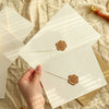 A hand is holding a set of linen texture retro envelopes with sealing wax stickers on a light fabric background.