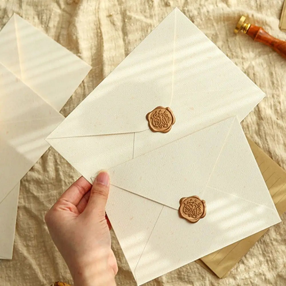 A hand is holding a set of linen texture retro envelopes with sealing wax stickers on a light fabric background.