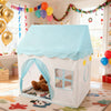 A white playhouse tent with a light blue roof and arched entrance, decorated with balloons and festive garlands.