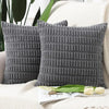 A pair of dark gray corduroy pillows with a textured striped velvet design resting on a white knitted surface.