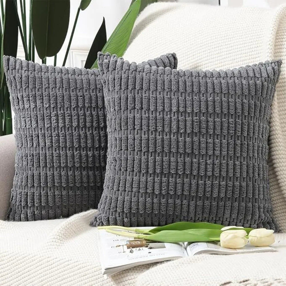 A pair of dark gray corduroy pillows with a textured striped velvet design resting on a white knitted surface.