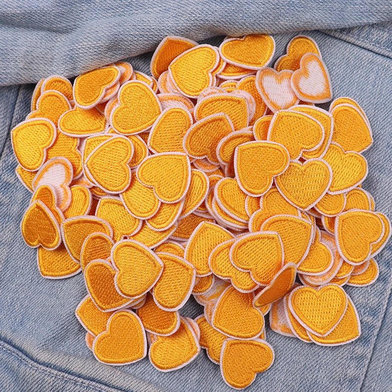 A cluster of orange and cream heart-shaped embroidered iron-on patches on a denim fabric.