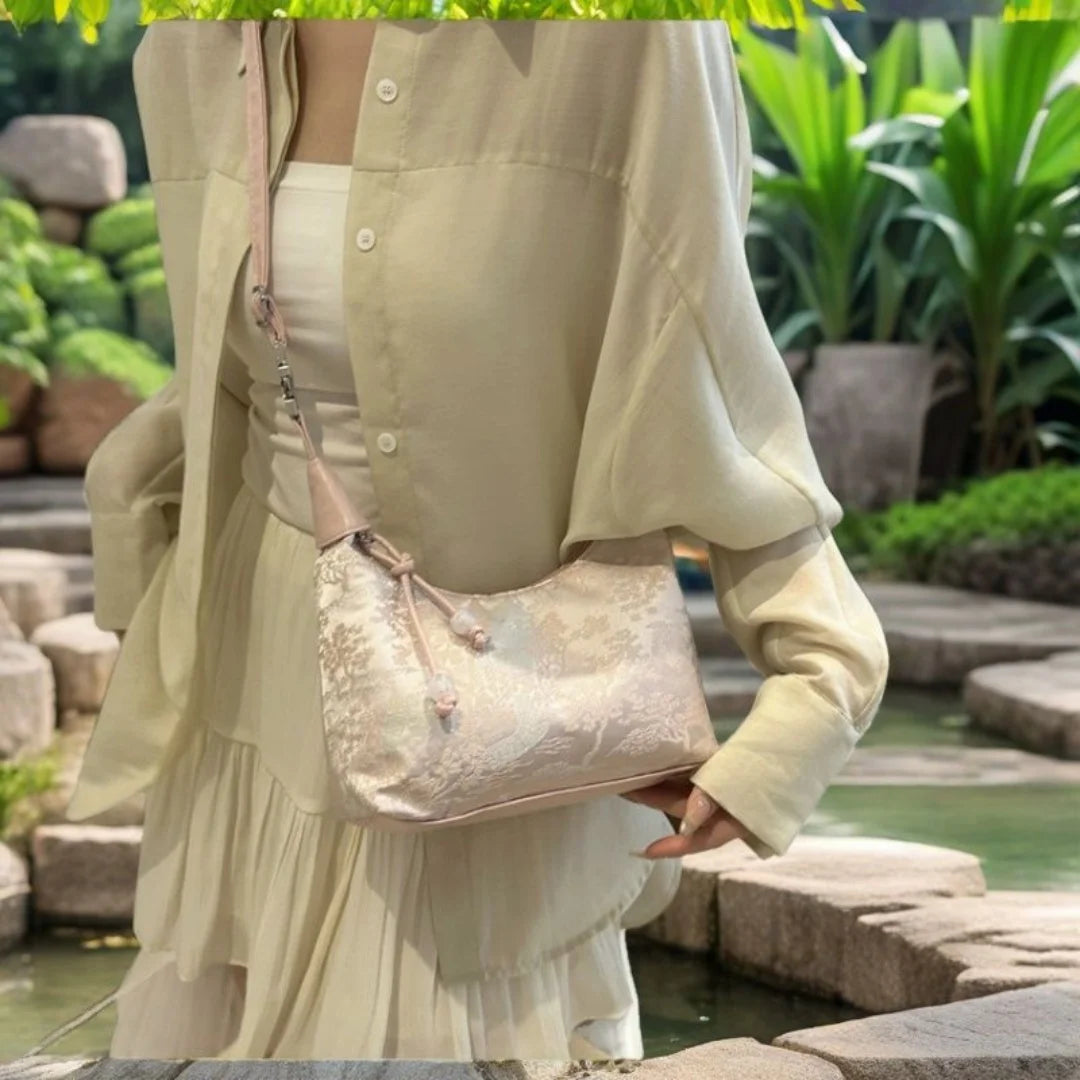 Eine Frau in einem hellbeigen Kleid hält eine Perlenstickerei-Crossbodytasche im Vordergrund.