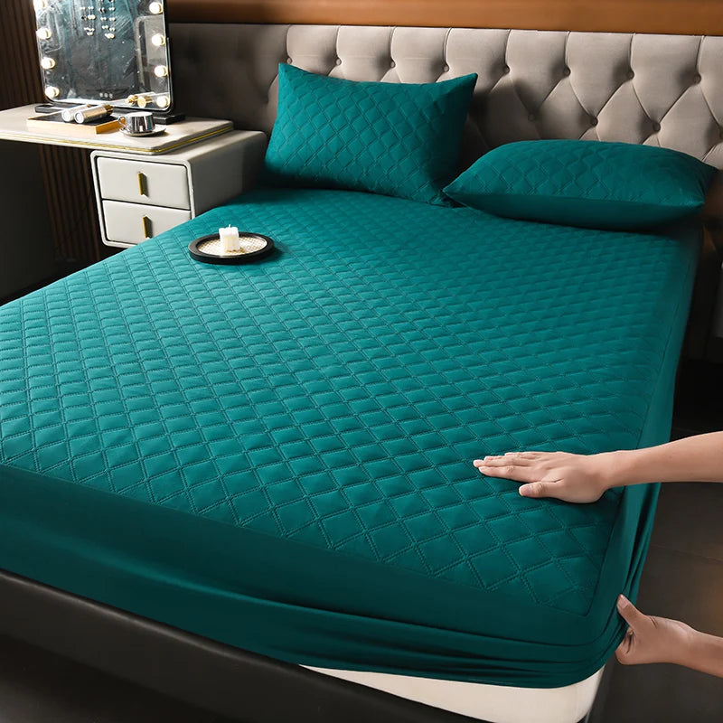A teal quilted mattress protector is shown on a bed, next to a headboard and a mirror.